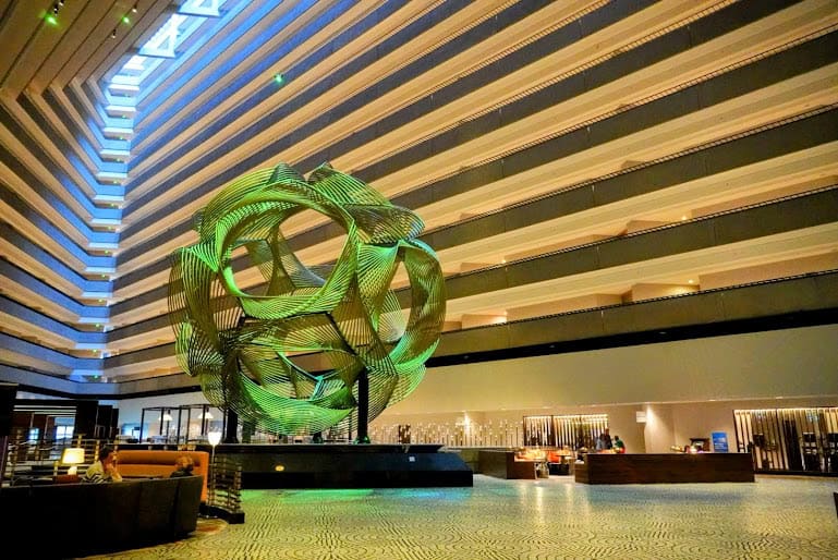 The stunning atrium of the Hyatt Regency San Francisco, highlighted by a geometric green sculpture at its center and surrounded by layers of modern architecture.