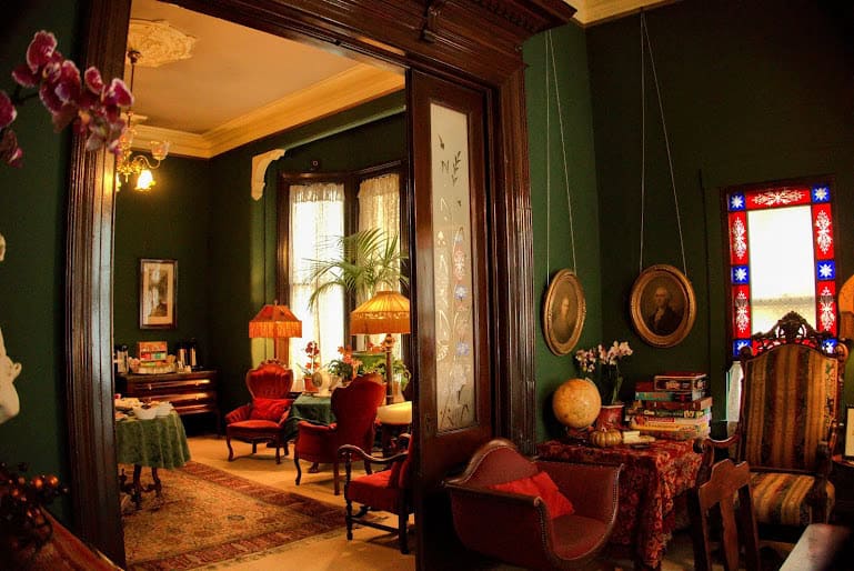 A cozy Victorian-style parlor at the Inn San Francisco, adorned with antique furniture, stained glass windows, and lush greenery, offering a nostalgic glimpse of old-world charm.