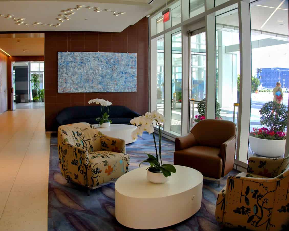 A chic seating area at the LUMA Hotel in San Francisco, featuring modern armchairs, a coffee table with orchids, and contemporary art in a bright and airy setting with floor-to-ceiling windows.