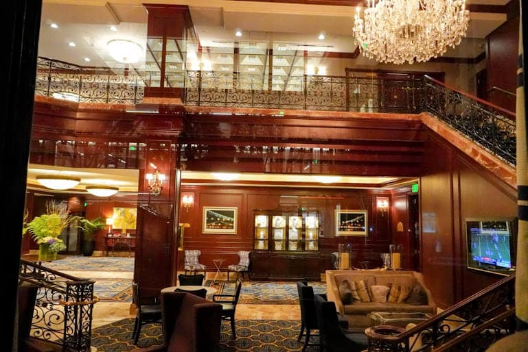The Omni San Francisco’s luxurious lobby, featuring rich wood paneling, a grand staircase, and elegant chandeliers for a classic, upscale ambiance.