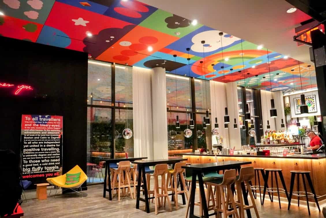 The vibrant and playful bar area of citizenM San Francisco, featuring colorful ceiling art, modern furnishings, and a relaxed, creative vibe.
