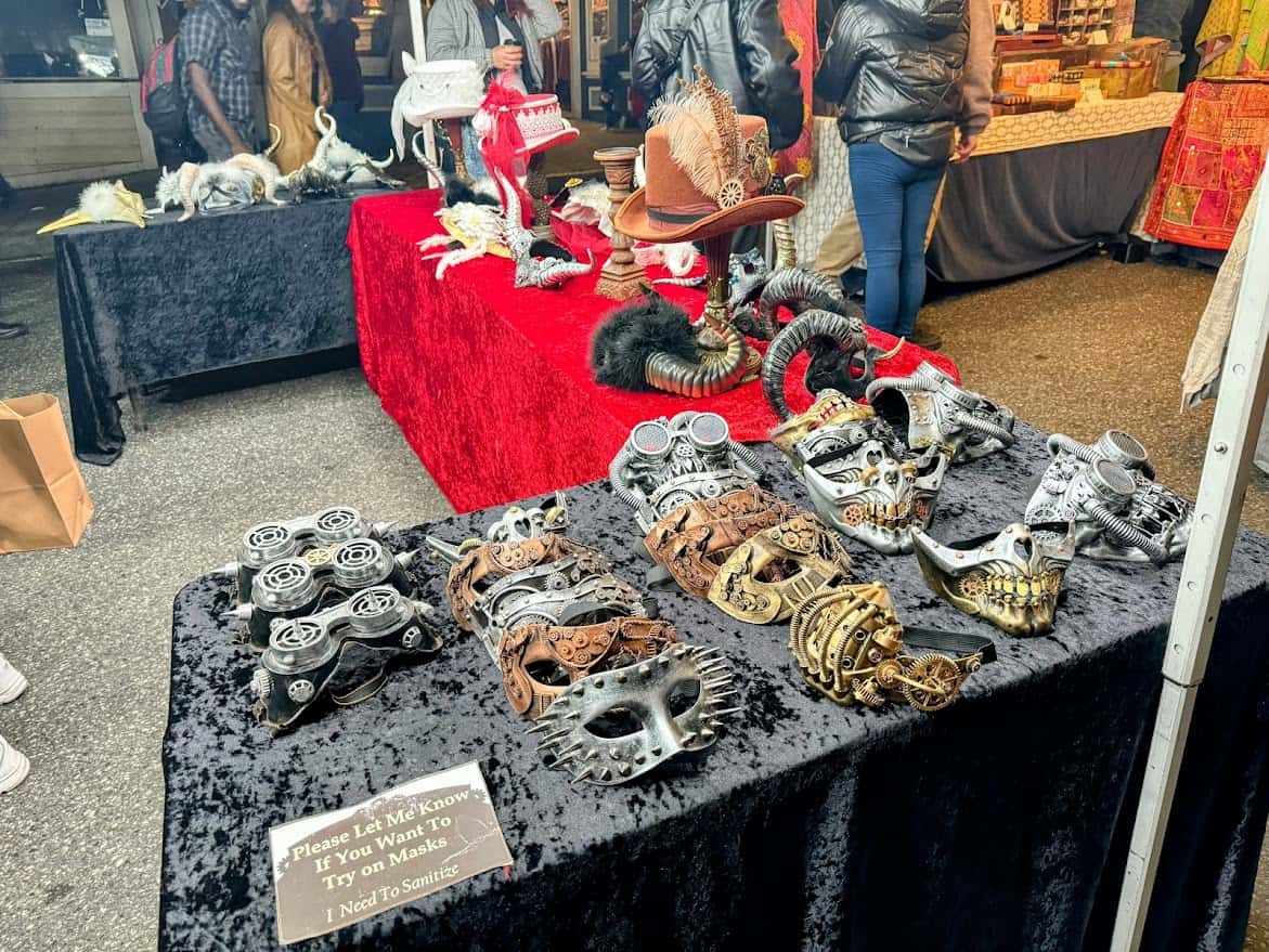 A vendor table displaying steampunk and Victorian-inspired masks at the Nevada City Victorian Christmas. Intricately designed masks with gears and metallic details are showcased on black velvet.