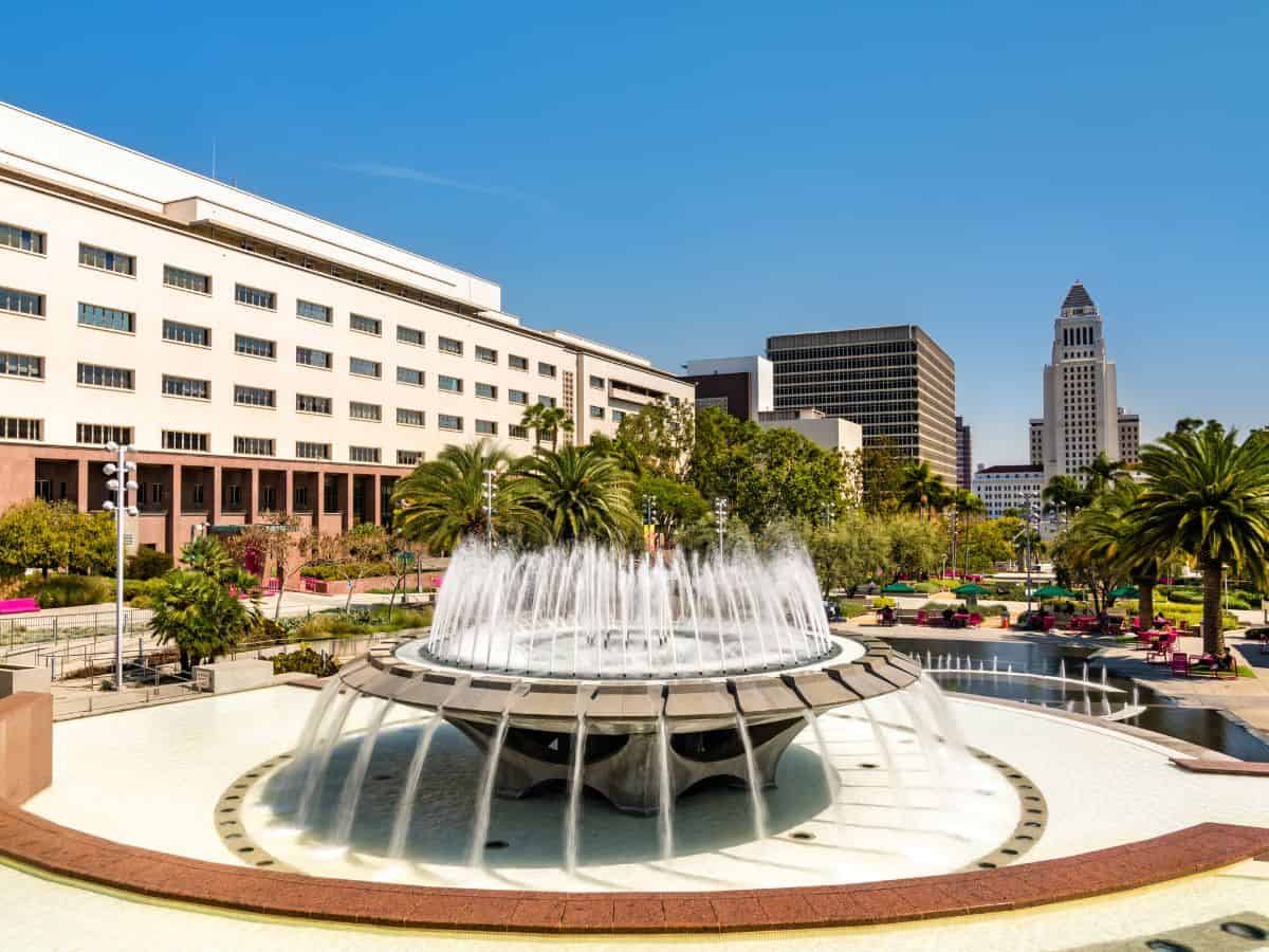 A large fountain with water cascading in front of a government building, surrounded by palm trees and greenery.