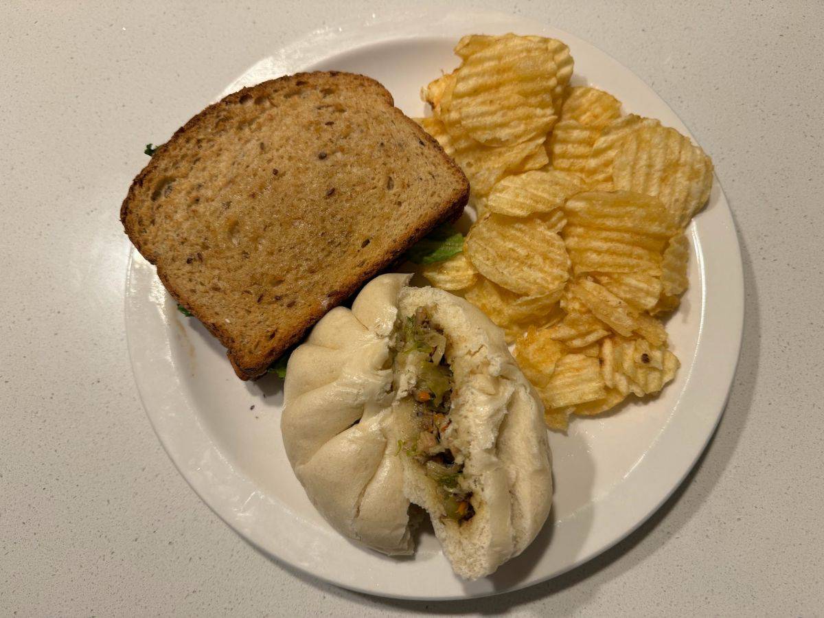 A delightful vegan lunch plate featuring a whole grain sandwich filled with fresh greens, a fluffy steamed bun stuffed with a savory vegetable mixture, and a side of crispy potato chips. This wholesome and comforting meal is a great example of offerings from one of the 10 Vegan Spots in San Jose.