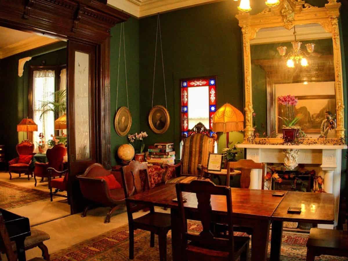 An elegant and richly decorated Victorian-style interior with ornate furniture, stained glass accents, and a grand gilded mirror above a detailed fireplace. The timeless charm and historic character of such spaces in San Francisco highlight the preservation of architectural heritage, raising the question, Why Is San Francisco So Expensive, as maintaining and restoring these iconic homes contributes to the city's high living costs.