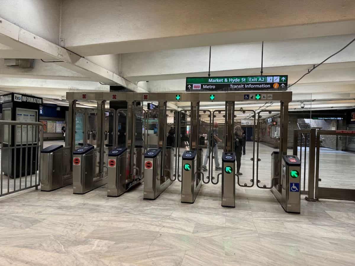The entrance to a San Francisco BART station with modern turnstiles and signage directing passengers to Market & Hyde Street. The clean yet utilitarian design highlights the city's public transportation infrastructure, raising the question, Why Is San Francisco So Expensive, as limitations in transit options and accessibility contribute to increased reliance on costly alternatives like rideshares or personal vehicles.