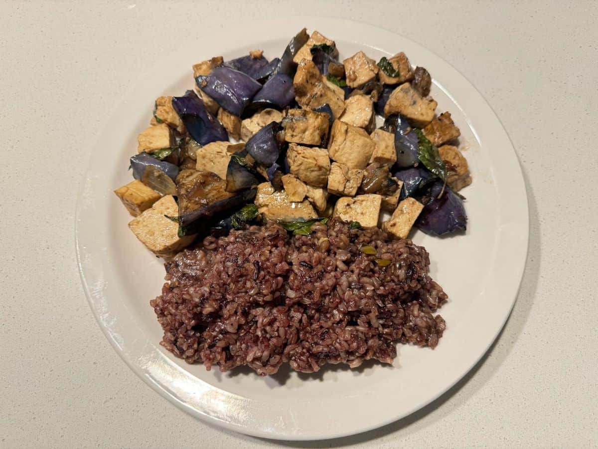 A vibrant plate of tofu stir-fried with eggplant and basil, paired with a portion of hearty purple rice, showcasing a flavorful vegan dish. This could be a signature offering from one of the 10 Vegan Spots in San Jose.