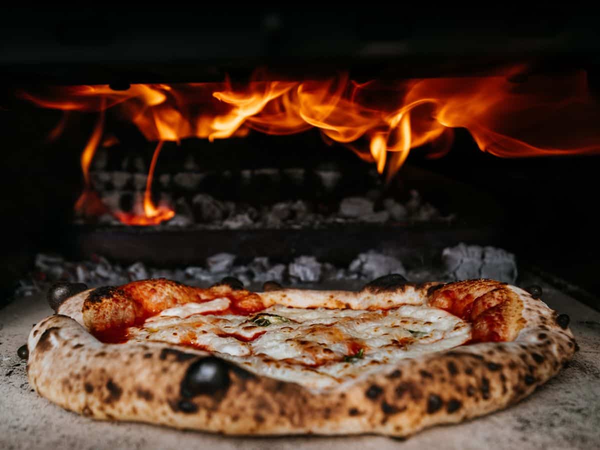 A Neapolitan pizza baking in a wood-fired oven, flames flickering in the background, and cheese bubbling on the crust.