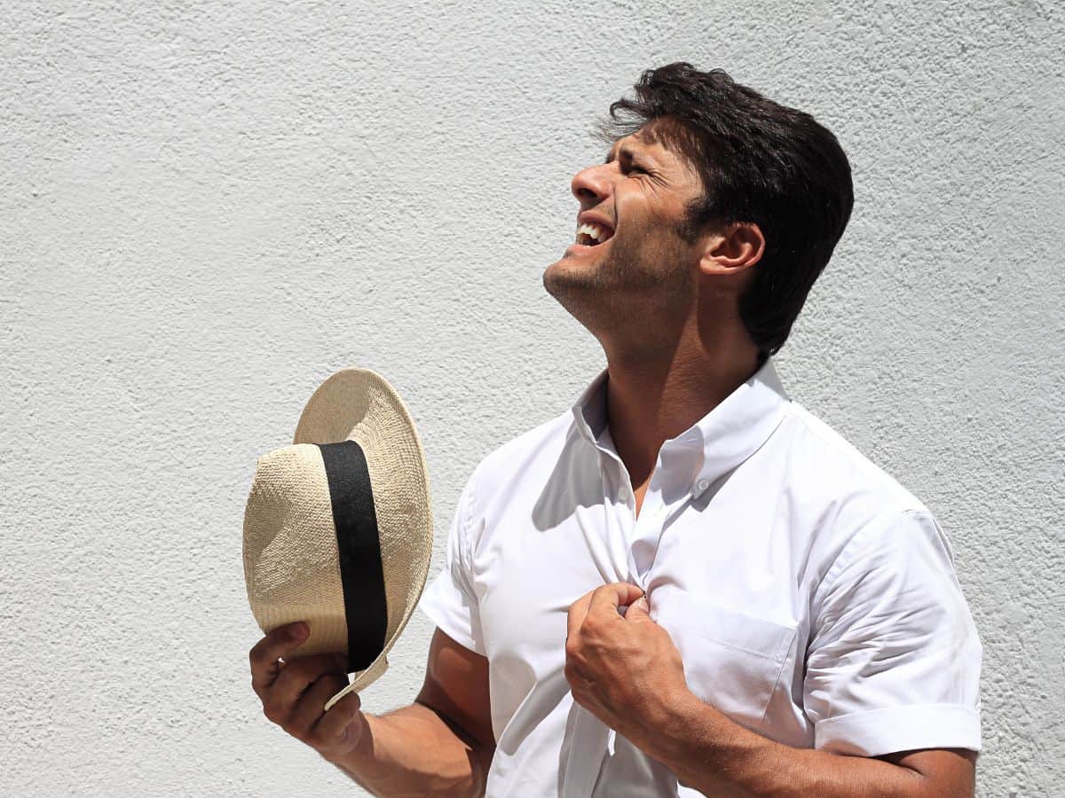 A man dressed in a white shirt holds a straw hat and squints against the intense sunlight, his expression reflecting discomfort from the heat. The image symbolizes the sunny, warm climate of Los Angeles, an attractive yet challenging feature that adds to the lifestyle costs and raises the question: Why Is Los Angeles So Expensive? The Truth About the High Costs of Living.
