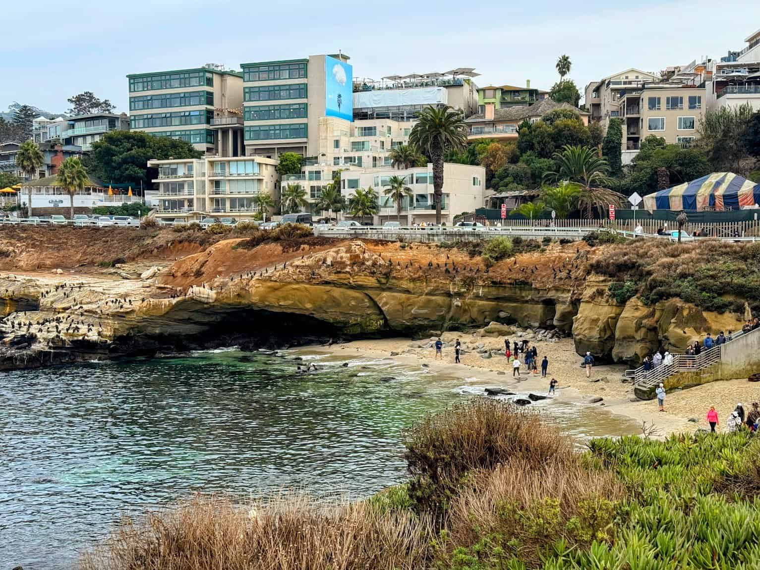 A small, sheltered beach with clear blue waters, surrounded by cliffs and vibrant greenery.