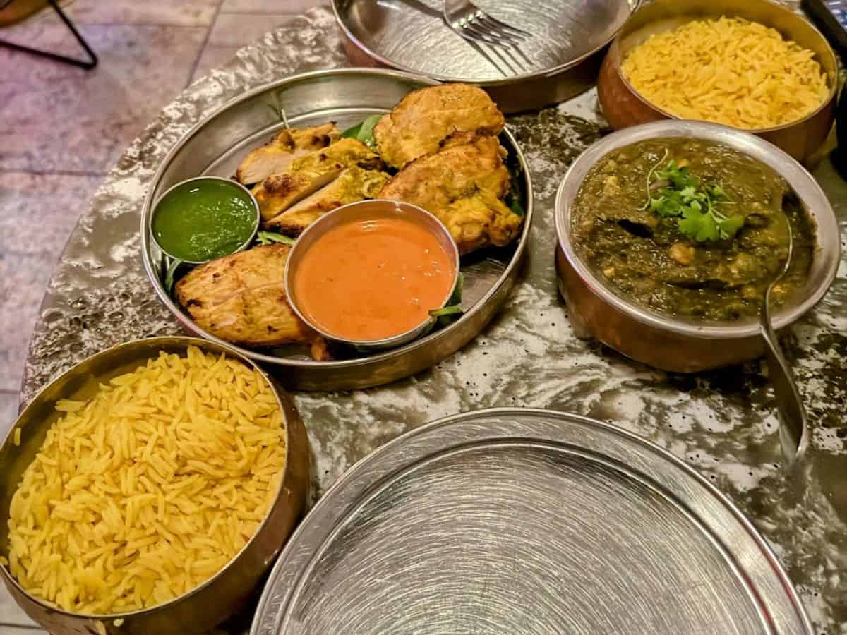 A spread of Indian cuisine served in traditional metal dishes, featuring chicken, creamy curries, and fragrant yellow rice. The rich colors and textures make the meal look inviting.