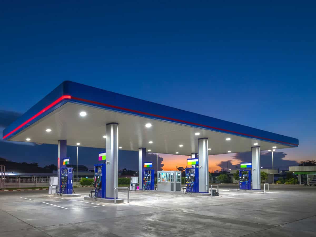 A modern gas station illuminated at twilight, with multiple fuel pumps under a sleek blue and red canopy, against a deep blue sky with hints of sunset.