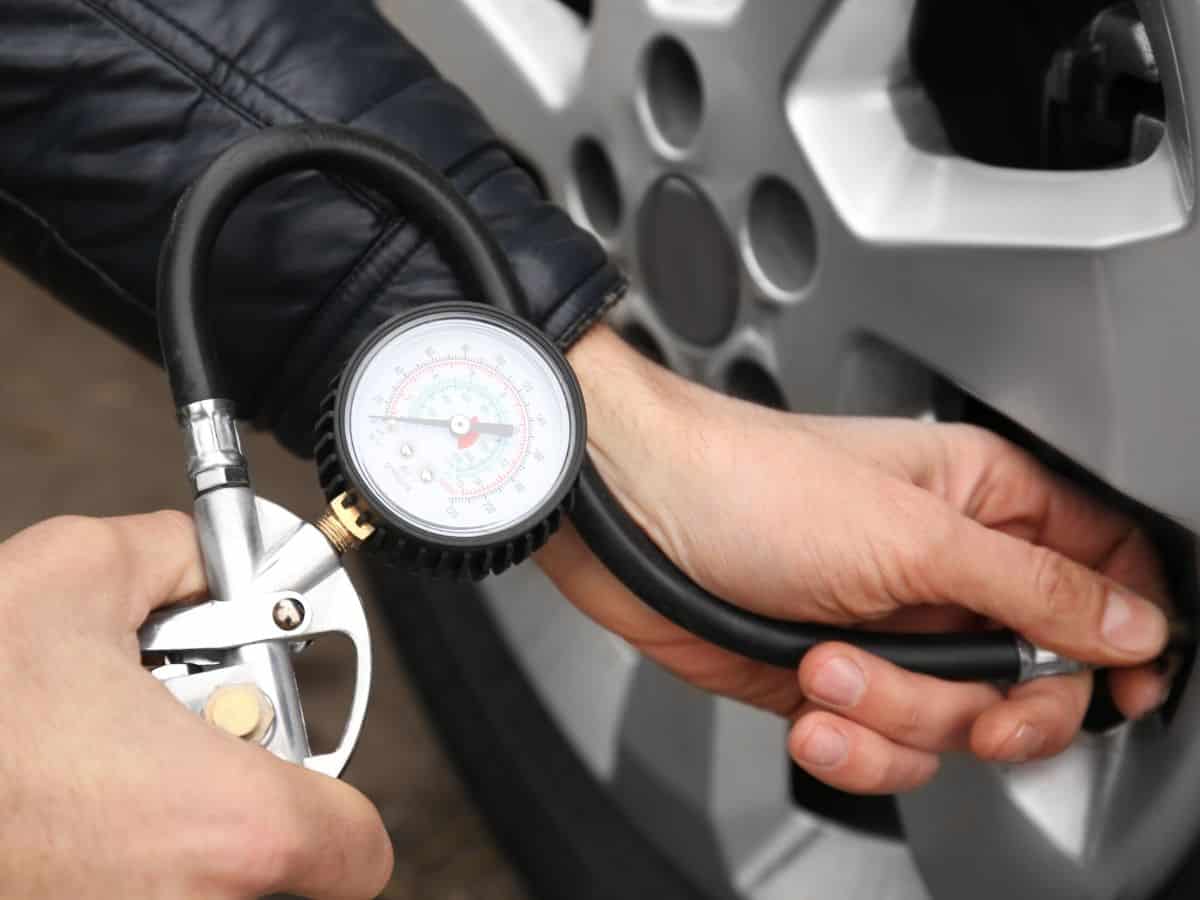 A close-up of a hand using a tire pressure gauge to check a car’s tire pressure, showing the gauge needle pointing to a measurement.