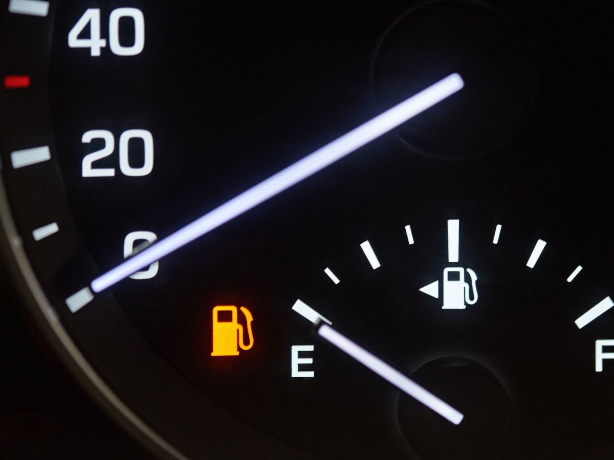 A close-up of a car’s fuel gauge displaying a nearly empty tank, with the orange low fuel warning light illuminated.