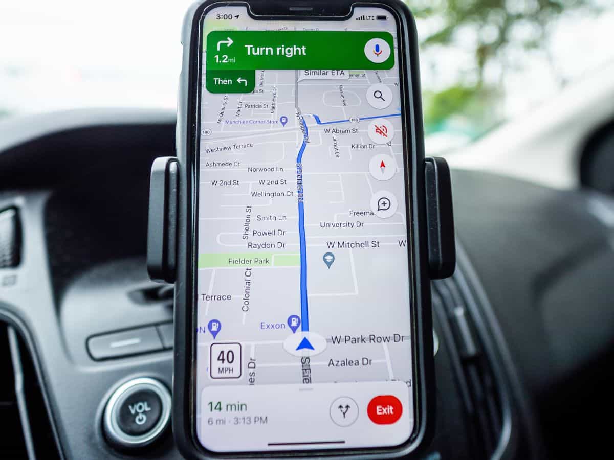 A smartphone mounted on a car dashboard displaying Google Maps navigation, showing a blue route line and turn-by-turn driving instructions.