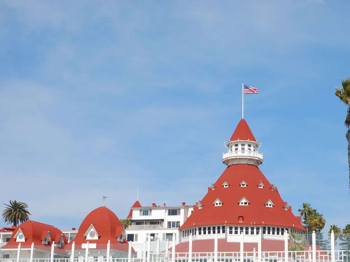 Iconic red-roofed turret of Hotel del Coronado in San Diego, California, with the American flag flying at the top against a clear blue sky.