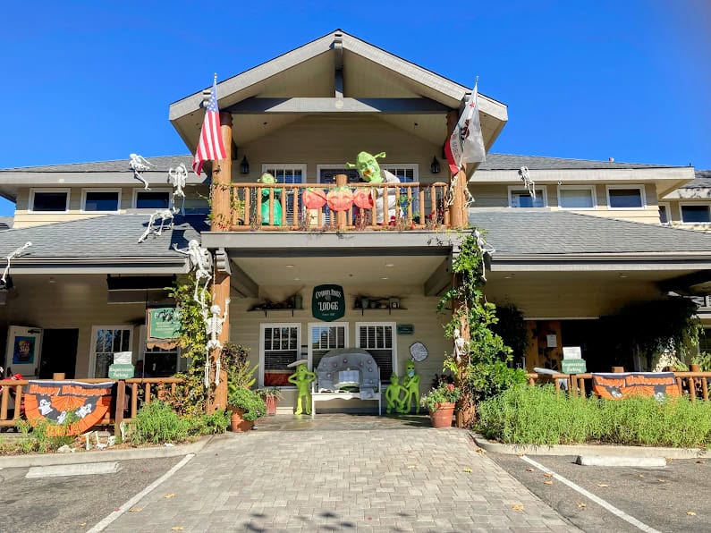 A charming lodge decorated for Halloween with skeletons, pumpkins, and green alien figures on the balcony. The American and California flags wave above the entrance.