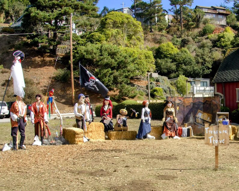 A pirate-themed display at Cambria’s Scarecrow Festival, featuring life-sized scarecrows dressed as pirates, a black flag with a skull, and a treasure trove sign.