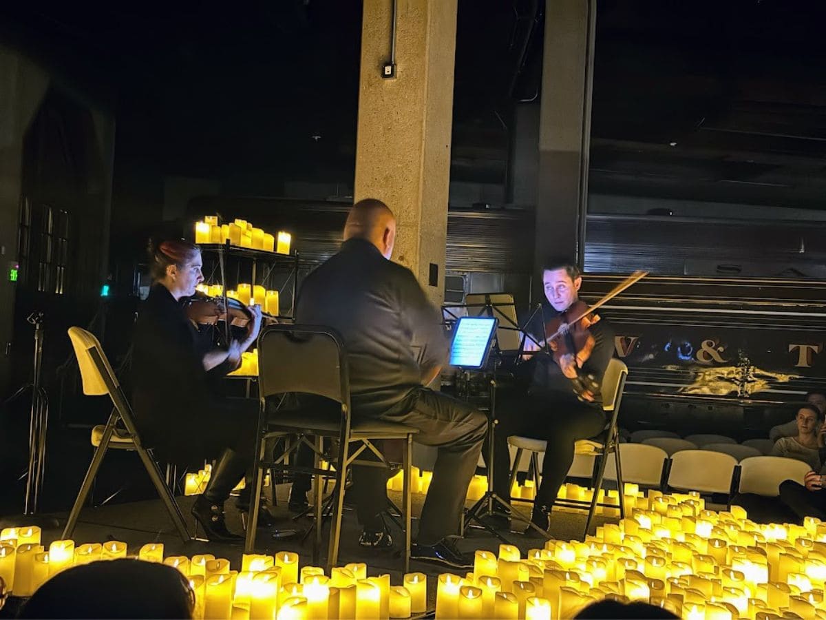 A candlelight concert with a string trio performing in an intimate, dimly lit setting surrounded by glowing candles, one of the unique picks from 32 Things To Do In Sacramento.