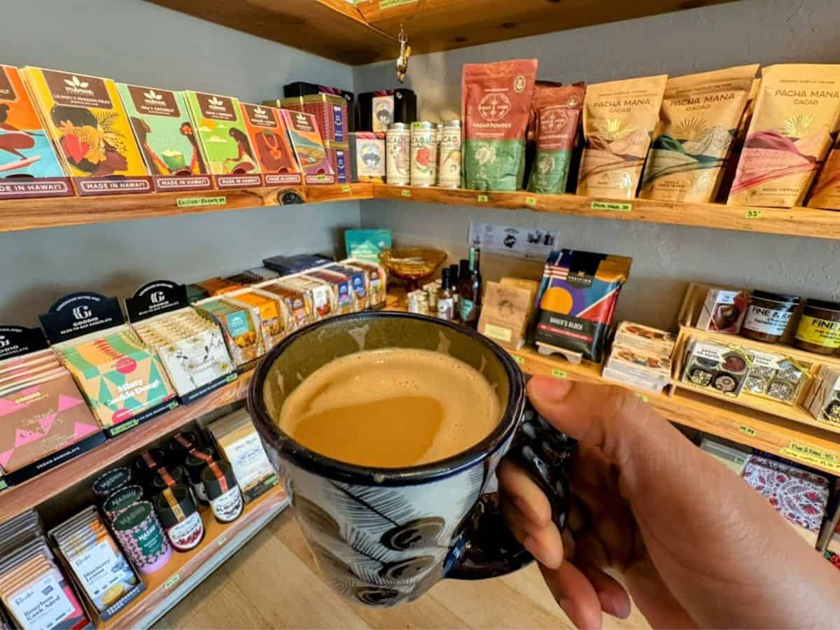 A hand holds a mug of hot chocolate inside a specialty chocolate shop filled with artisan bars and cacao products, a cozy pick from the 32 Things To Do In Sacramento.