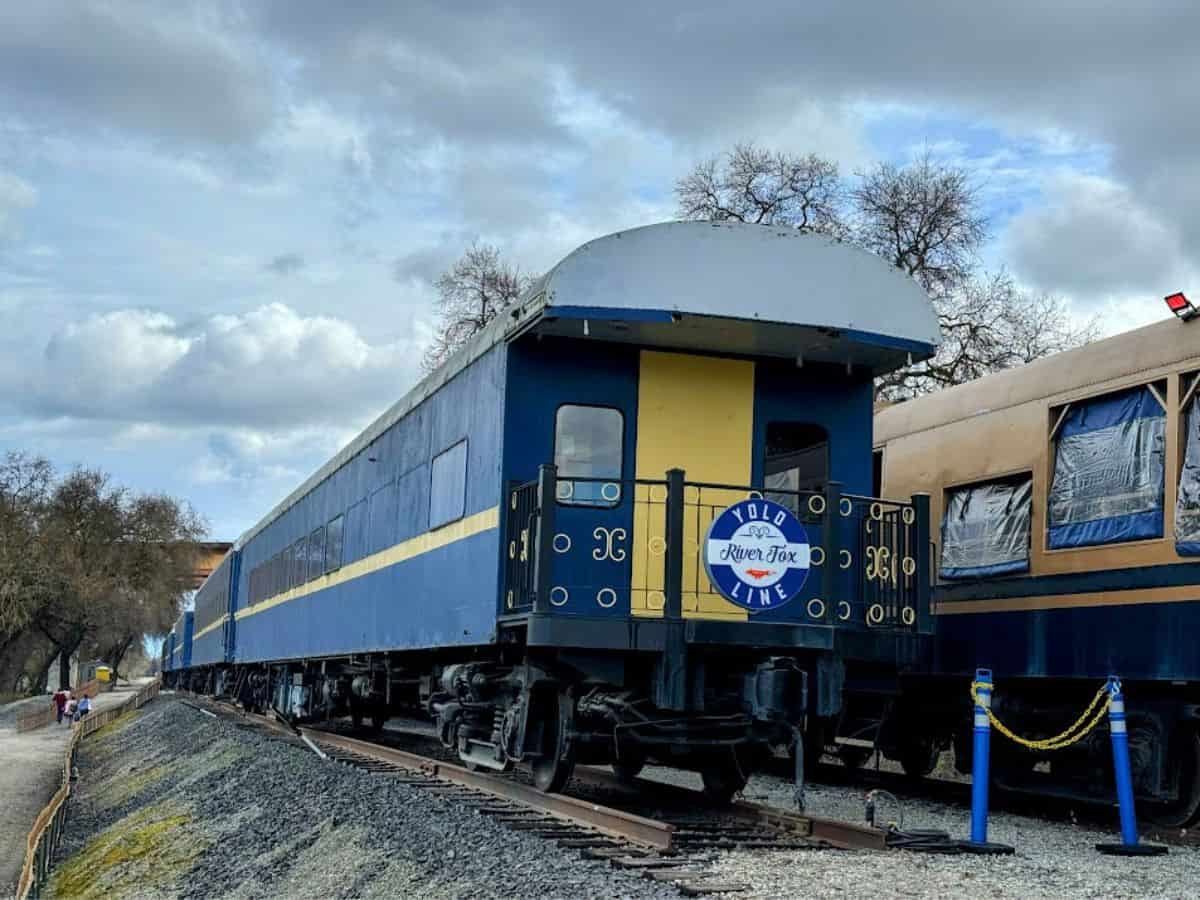 The Yolo River Fox Train with deep blue and yellow cars on a gravel-lined track, offering scenic rides featured in the 32 Things To Do In Sacramento.