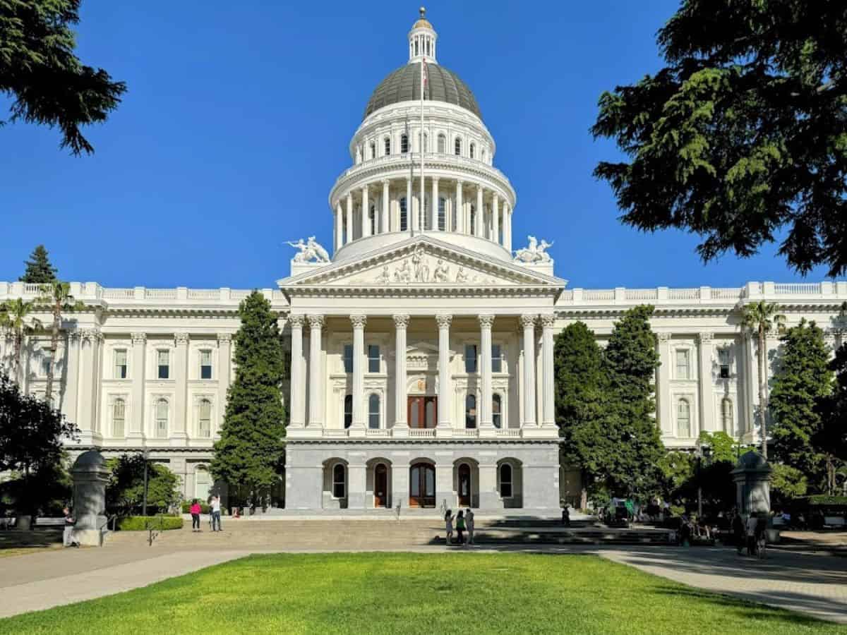 The California State Capitol building shines under a sunny sky, surrounded by trees and people exploring the grounds, as listed in 32 Things To Do In Sacramento.
