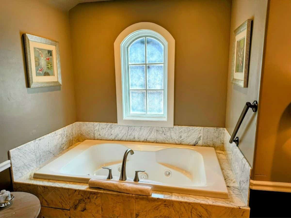 A luxurious marble bathtub with a curved window and soft lighting, offering a relaxing escape included in the 32 Things To Do In Sacramento for a cozy, pampered stay.