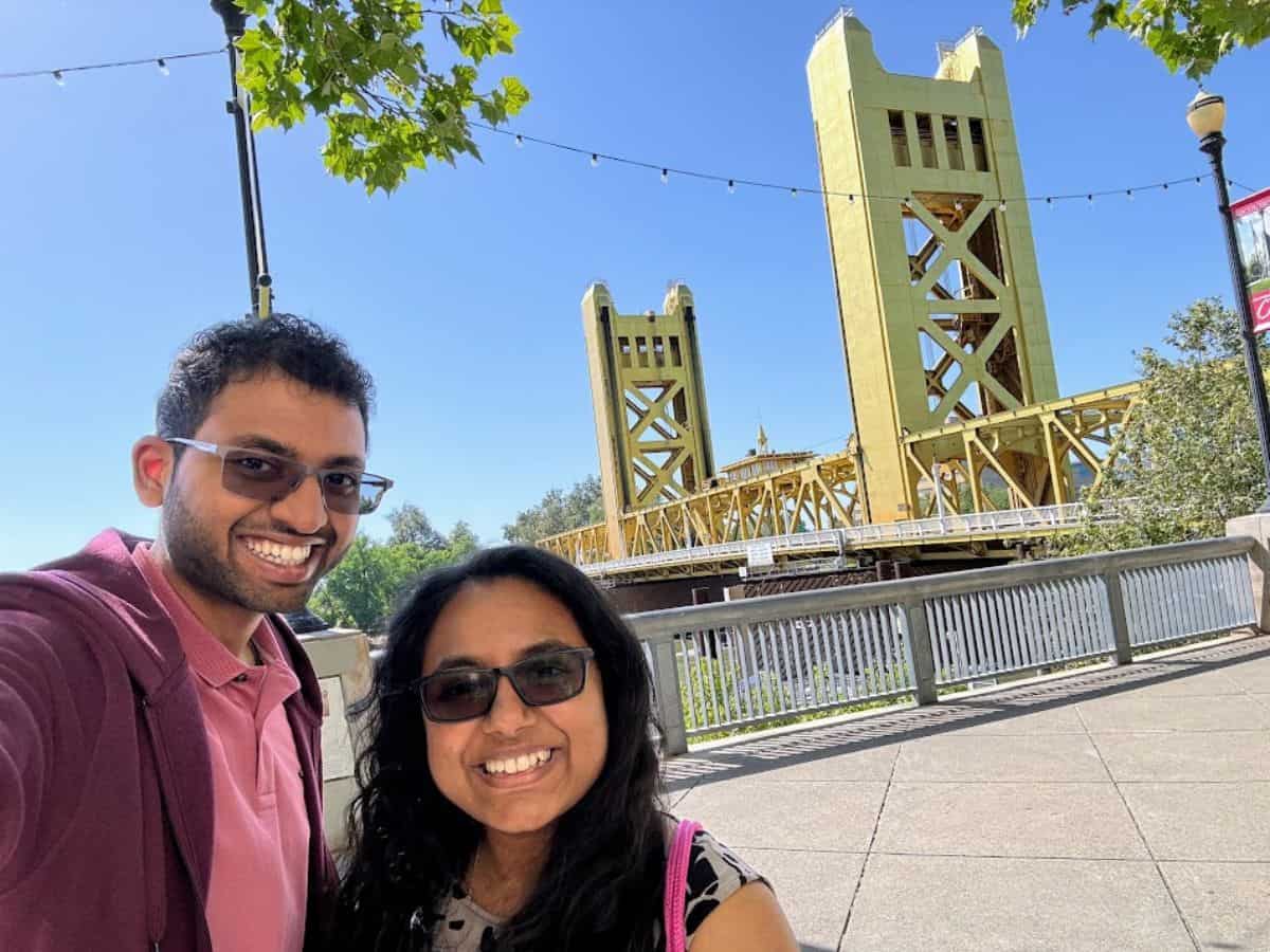 A smiling couple poses in front of the bright yellow Tower Bridge under a clear blue sky, one of the top spots featured in 32 Things To Do In Sacramento.