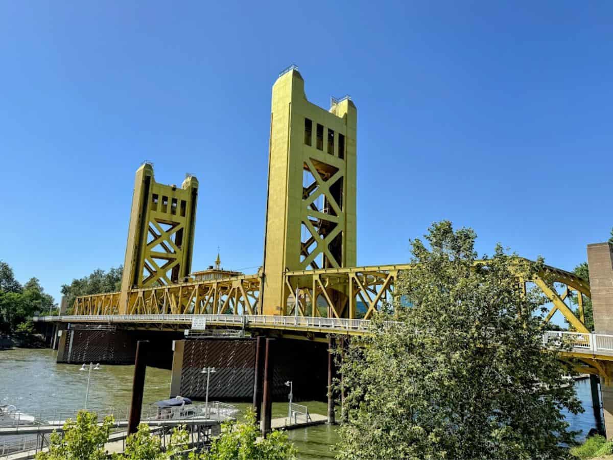 A wide shot of the yellow Tower Bridge stretching over the Sacramento River under a blue sky, featured prominently in 32 Things To Do In Sacramento.