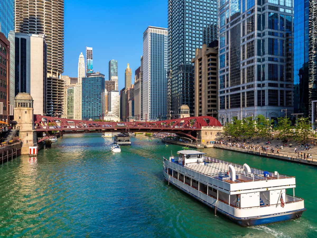 Daytime view of boats cruising down the Chicago River with stunning skyscrapers and a red bridge in the background—taking the Chicago Architecture River Cruise is one of the Top 10 Things to Do in Chicago, Ranked by Popularity.