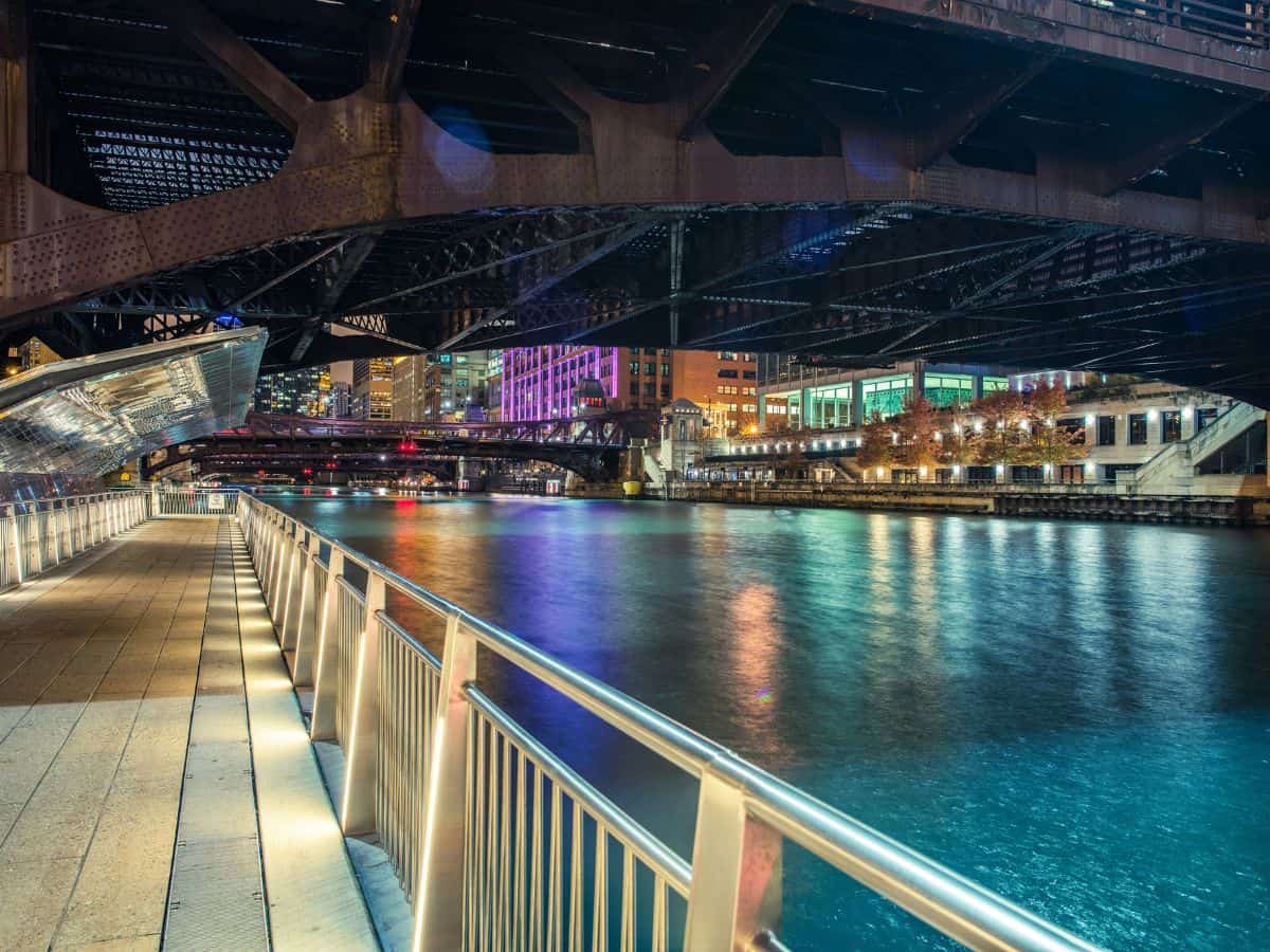 Scenic night view of the Chicago Riverwalk lit up under multiple bridges, reflecting colorful city lights—walking the Riverwalk is definitely among the Top 10 Things to Do in Chicago, Ranked by Popularity.