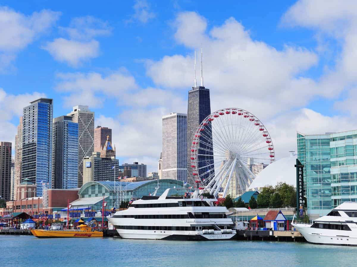 A sunny view of Navy Pier with boats docked near the water, a large Ferris wheel, and the Chicago skyline behind it—Navy Pier ranks high among the Top 10 Things to Do in Chicago, Ranked by Popularity.