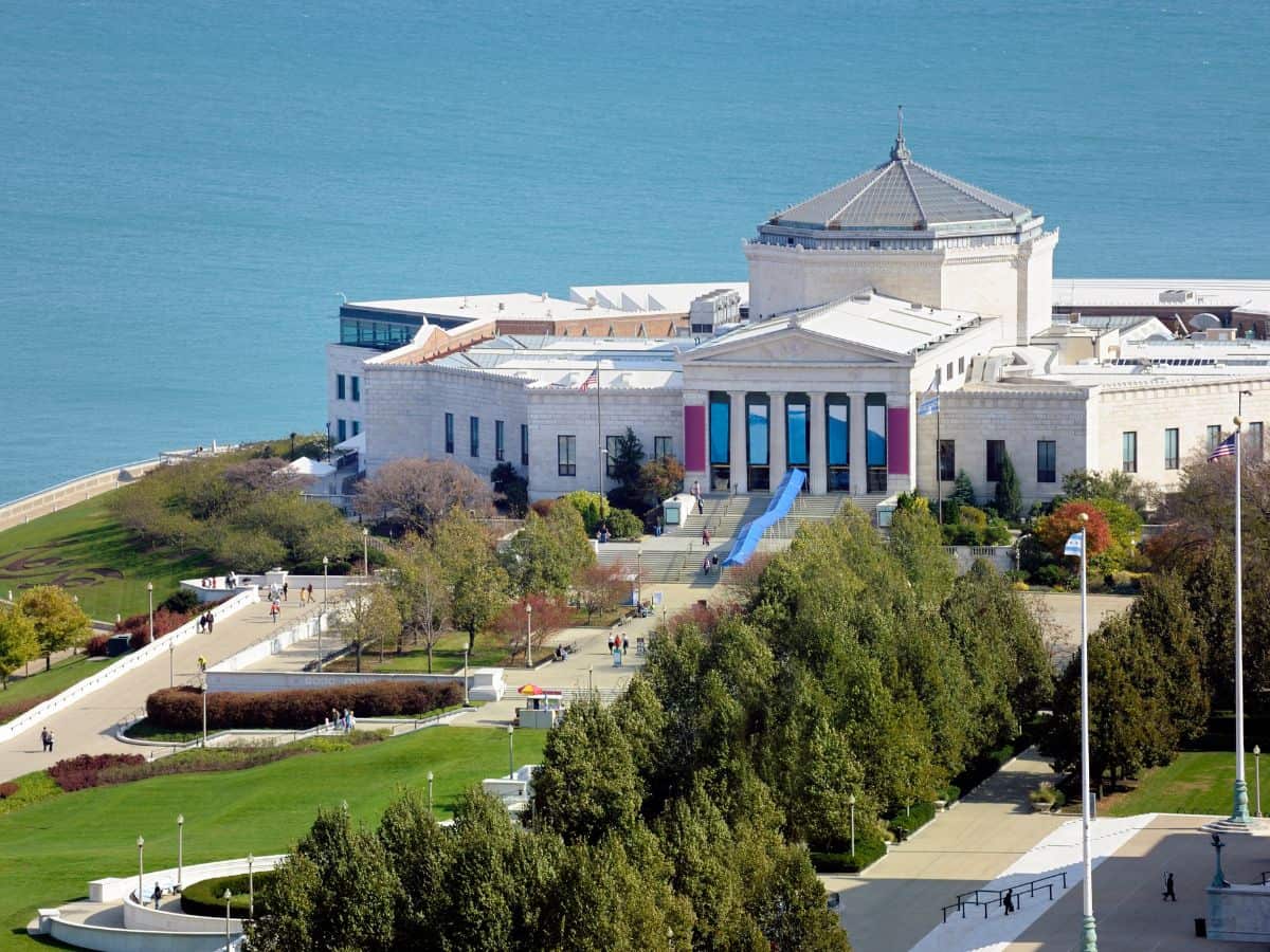 Aerial view of Shedd Aquarium located on the Lake Michigan shoreline with people walking around the green park—visiting this marine attraction is one of the Top 10 Things to Do in Chicago, Ranked by Popularity.