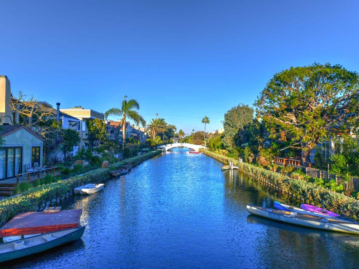 The charming Venice Canals in Los Angeles, with their peaceful waterways, lush greenery, and small boats, offer a picturesque scene similar to Venice, Italy.