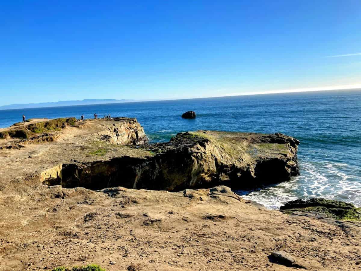A rugged coastal landscape with rocky cliffs and ocean waves stretching toward the horizon. Walking to Lighthouse Point to take in the dramatic ocean views is one of the best 21 Things to Do in Santa Cruz.