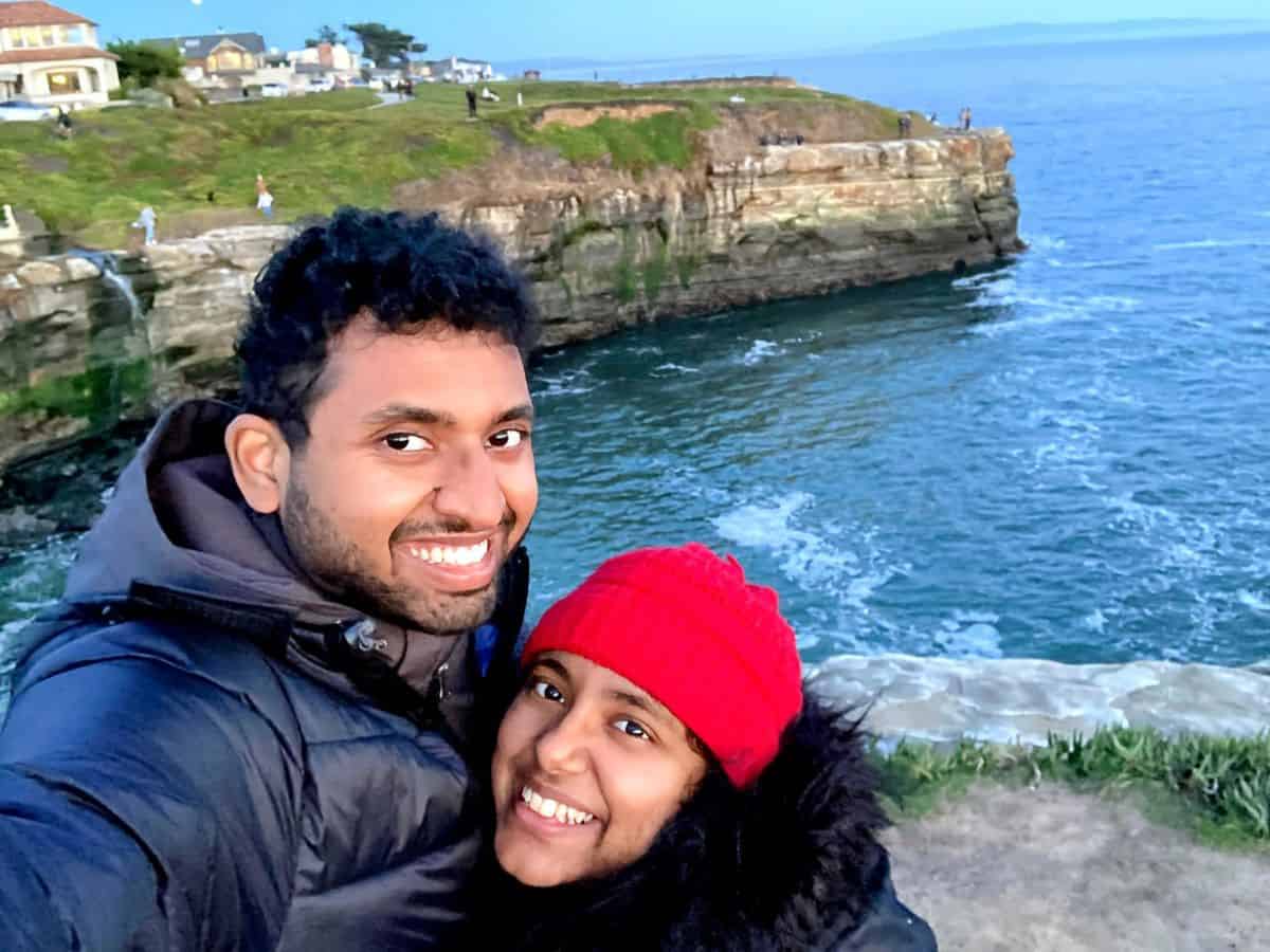 Kiran and Shreeyeh take a selfie with the stunning coastal cliffs of Santa Cruz in the background. One of the best 21 Things to Do in Santa Cruz is to enjoy breathtaking ocean views and take in the fresh sea air along the cliffs.