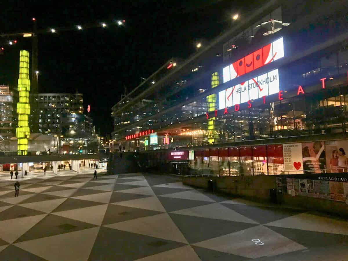 Sergels Torg, Stockholm’s modern central square, is lit up at night with geometric paving, a glowing green glass tower, and bright lights from Kulturhuset Stadsteatern.