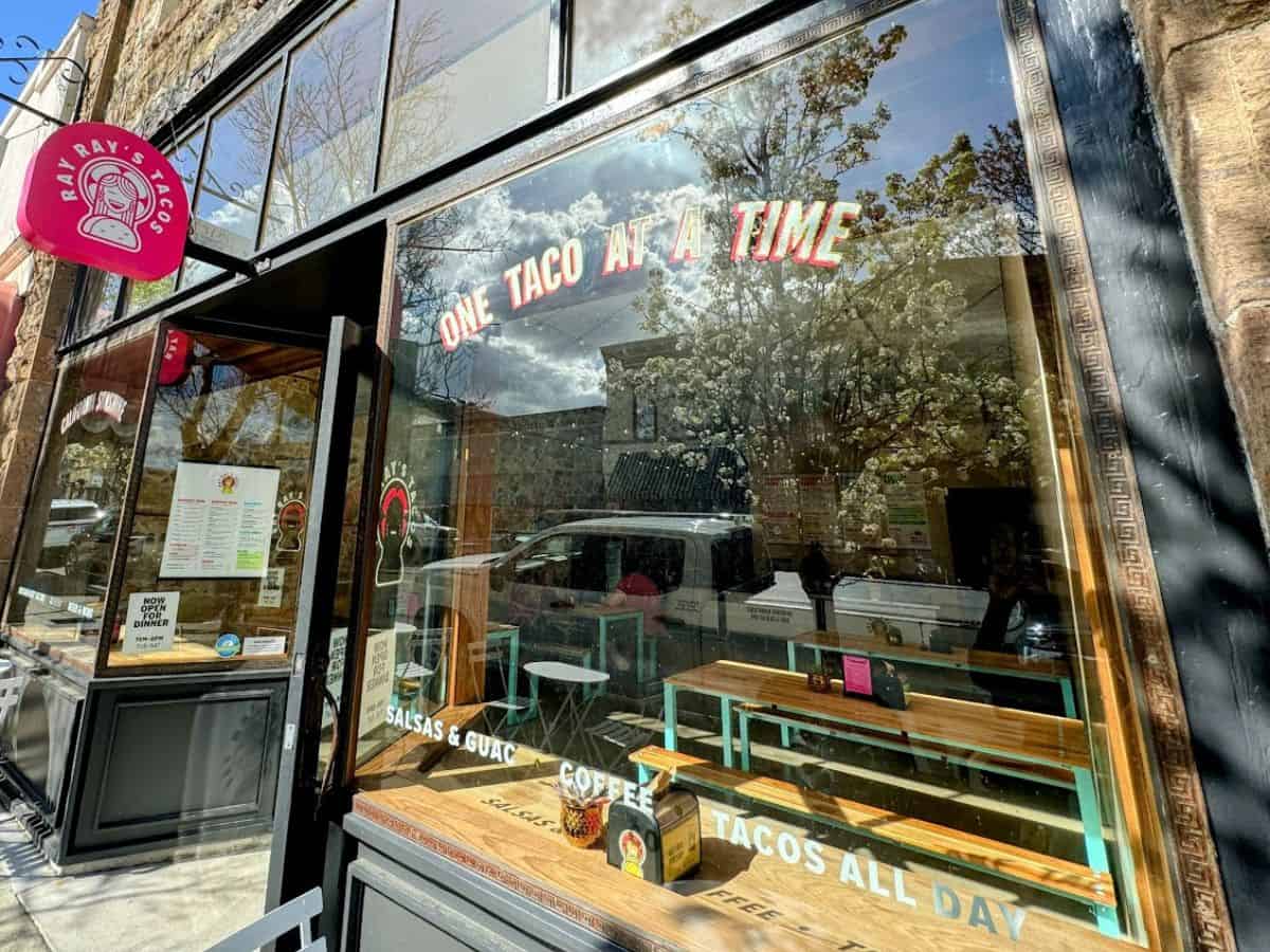 The storefront of Ray Ray’s Tacos with large windows reflecting spring blooms and a bold red sign reading “One Taco at a Time.” A lively, casual favorite for authentic eats among the 17 best places to eat in Napa Valley.