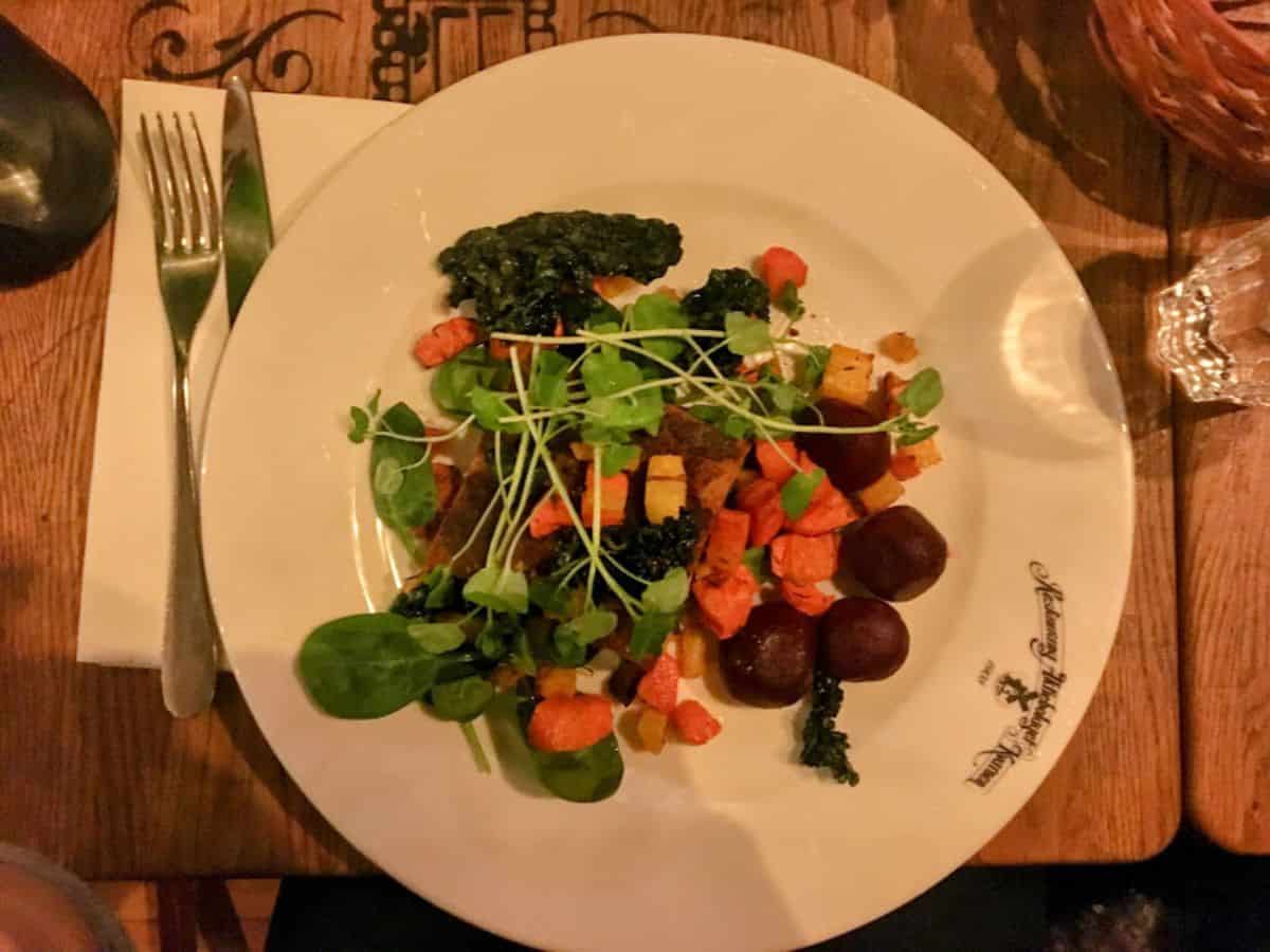 A plate of hearty, colorful root vegetables garnished with greens and sprouts, served on elegant white dishware at a traditional restaurant setting.