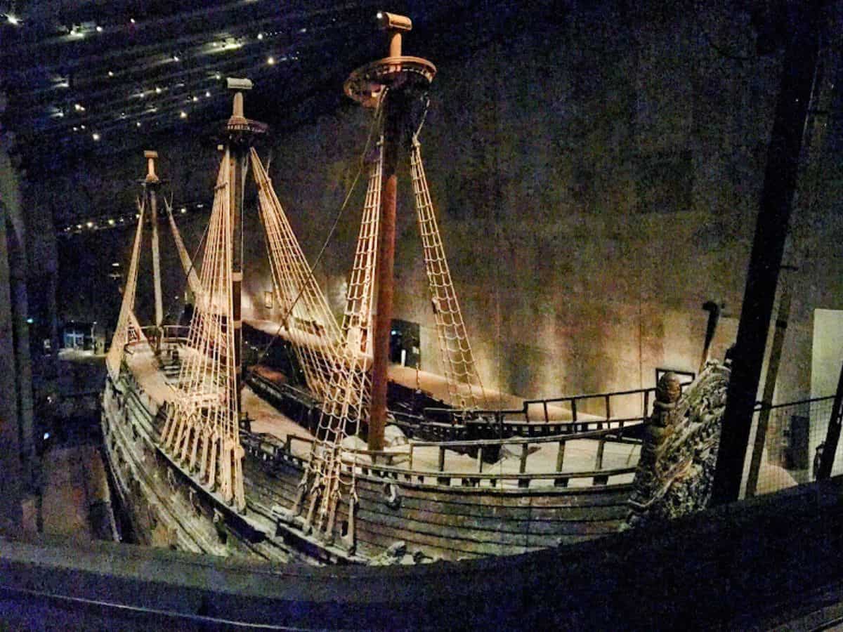The massive 17th-century Vasa warship, preserved inside a dimly lit museum, displays its intricate wooden structure and towering masts with rigging intact.