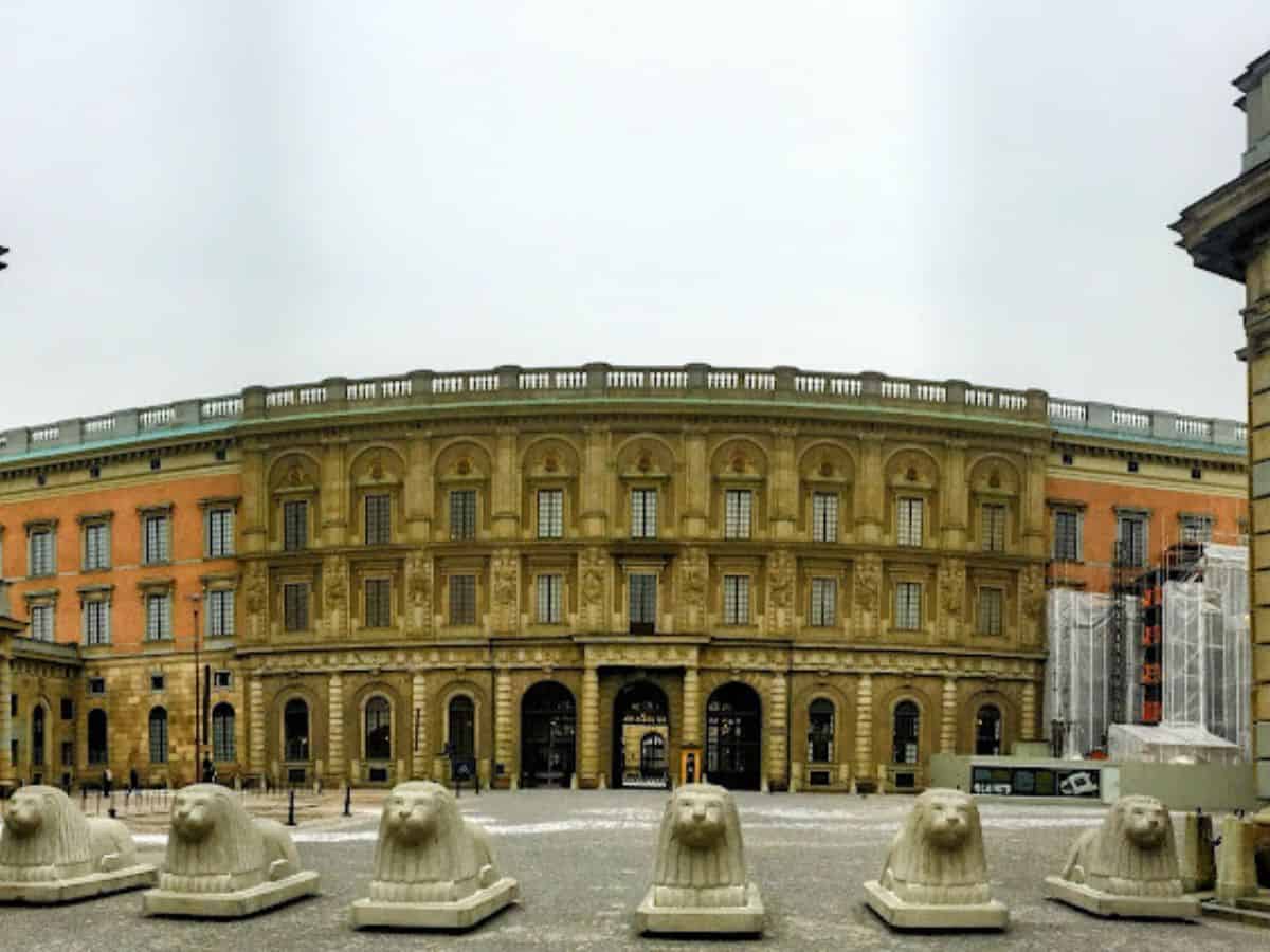The grand facade of Stockholm's Royal Palace, built in a classical style with a curved central section and lion statues in the foreground on a gray winter day.