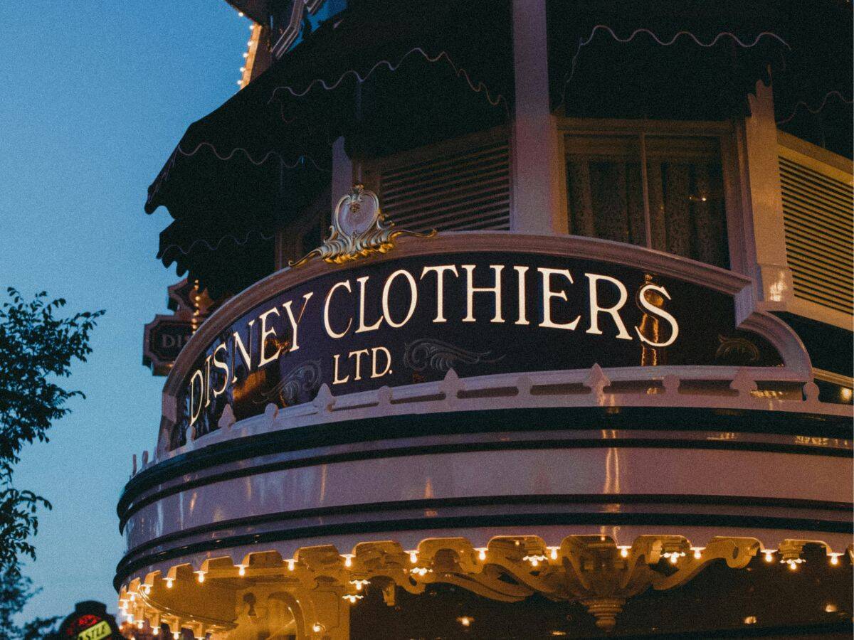 Close-up of the Disney Clothiers sign on Main Street U.S.A., illuminated at dusk with vintage-inspired lettering and festive lights.
