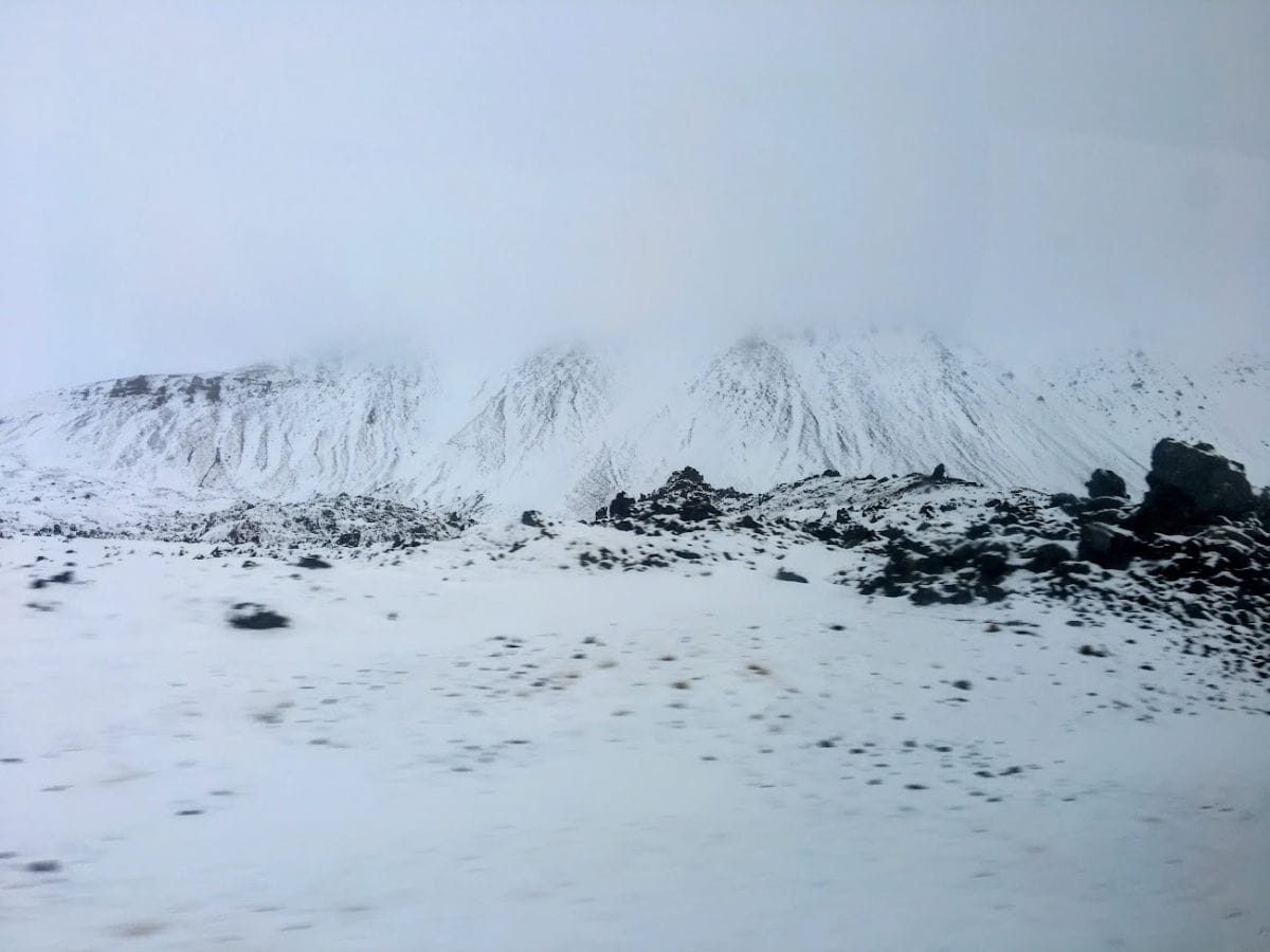 Jagged volcanic rocks and snow-covered ridges stretch into the mist, creating a stark and dramatic landscape. My Snowy Iceland Trip Was Equal Parts Stunning and Chaotic - Here's How to Be Ready for hauntingly beautiful terrain.