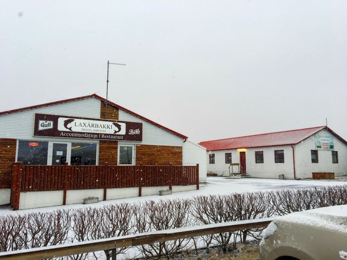 A cozy travel lodge named Laxárbakki sits quietly as snow falls outside, with red roofs adding contrast. My Snowy Iceland Trip Was Equal Parts Stunning and Chaotic - Here's How to Be Ready by booking your stay in advance before roads get sketchy.