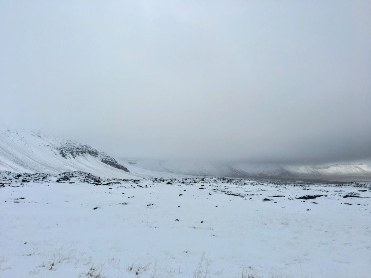 A vast, snow-covered valley fades into thick fog as low clouds obscure distant mountains. My Snowy Iceland Trip Was Equal Parts Stunning and Chaotic - Here's How to Be Ready when visibility vanishes and plans go with it.