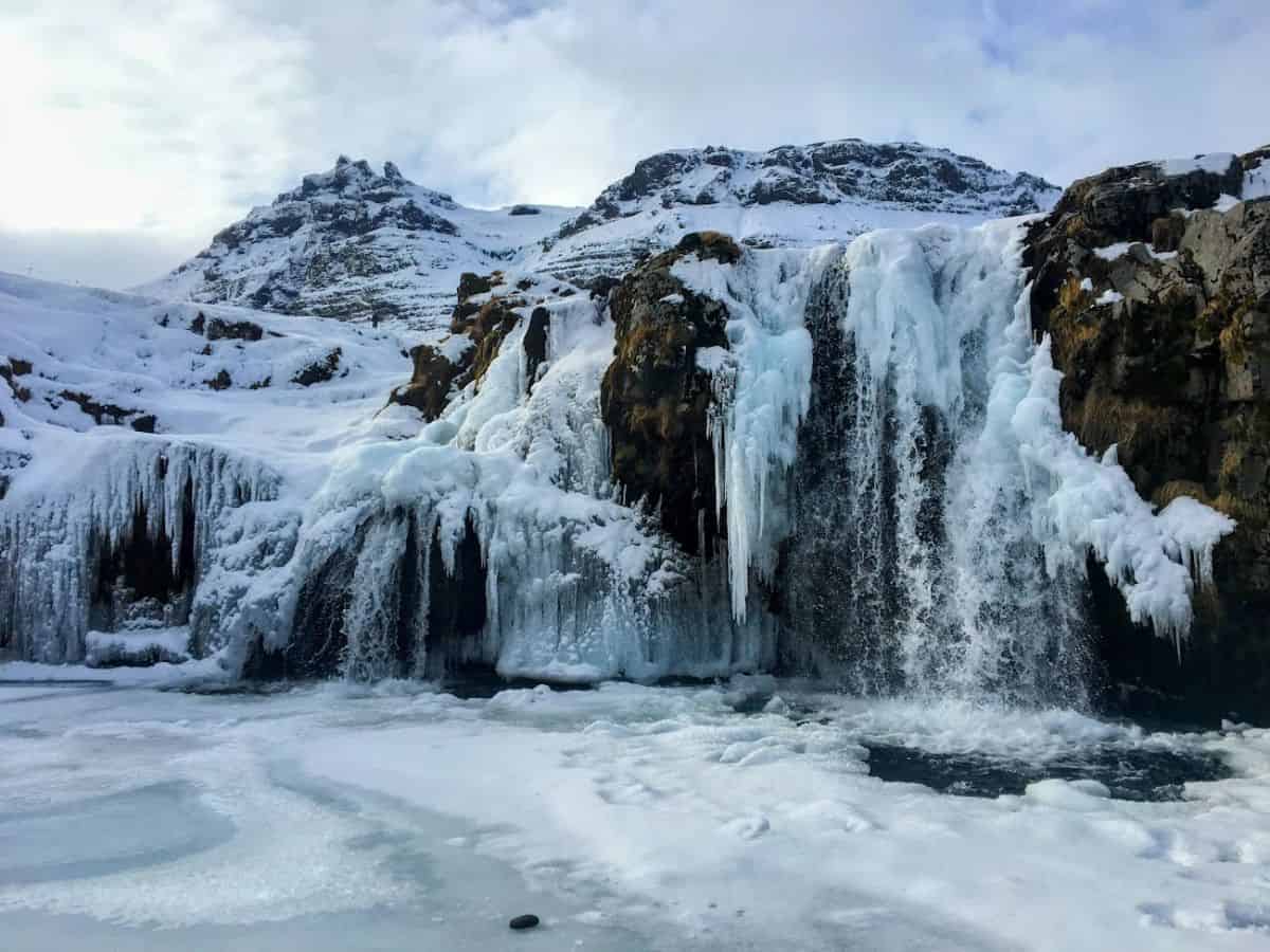 A stunning waterfall partially frozen mid-cascade, surrounded by thick snow and jagged mountains. My Snowy Iceland Trip Was Equal Parts Stunning and Chaotic - Here's How to Be Ready for icy beauty that stops you in your tracks—literally.