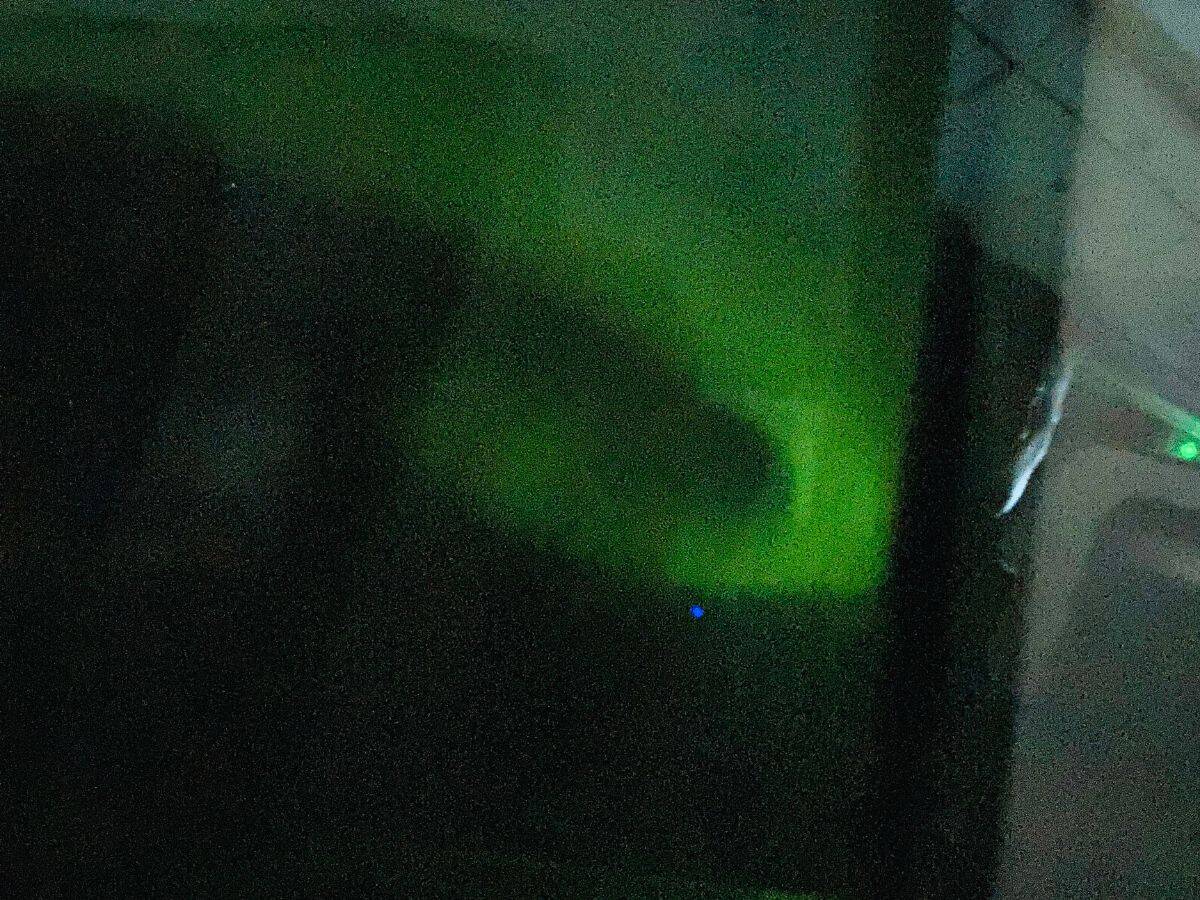 A faint green glow of the Northern Lights peeks through a grainy, dark sky, captured from a moving vehicle. My Snowy Iceland Trip Was Equal Parts Stunning and Chaotic - Here's How to Be Ready for fleeting magic and blurry proof you saw it.