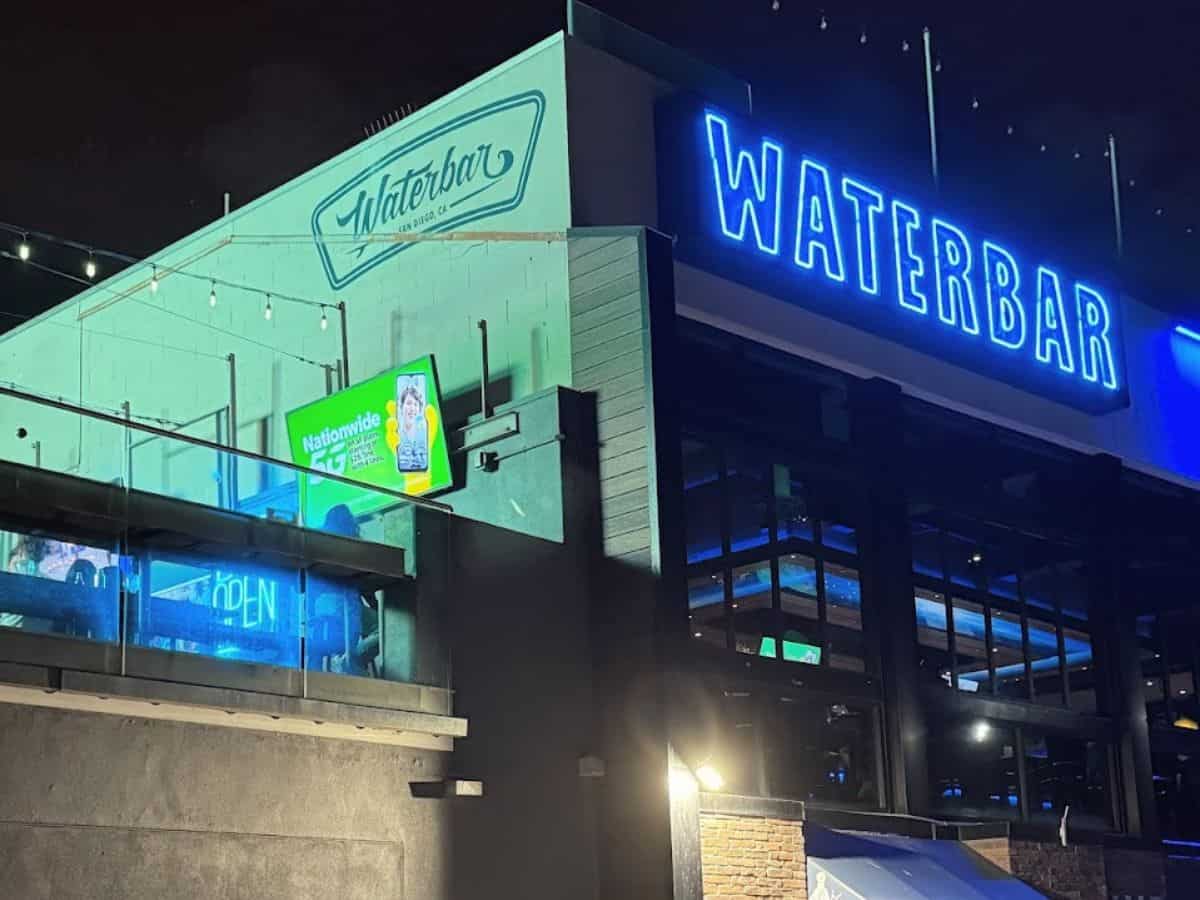 The exterior of Waterbar, one of the best restaurants in Pacific Beach San Diego, showcasing its modern facade with a vibrant blue 'WATERBAR' neon sign illuminating the night