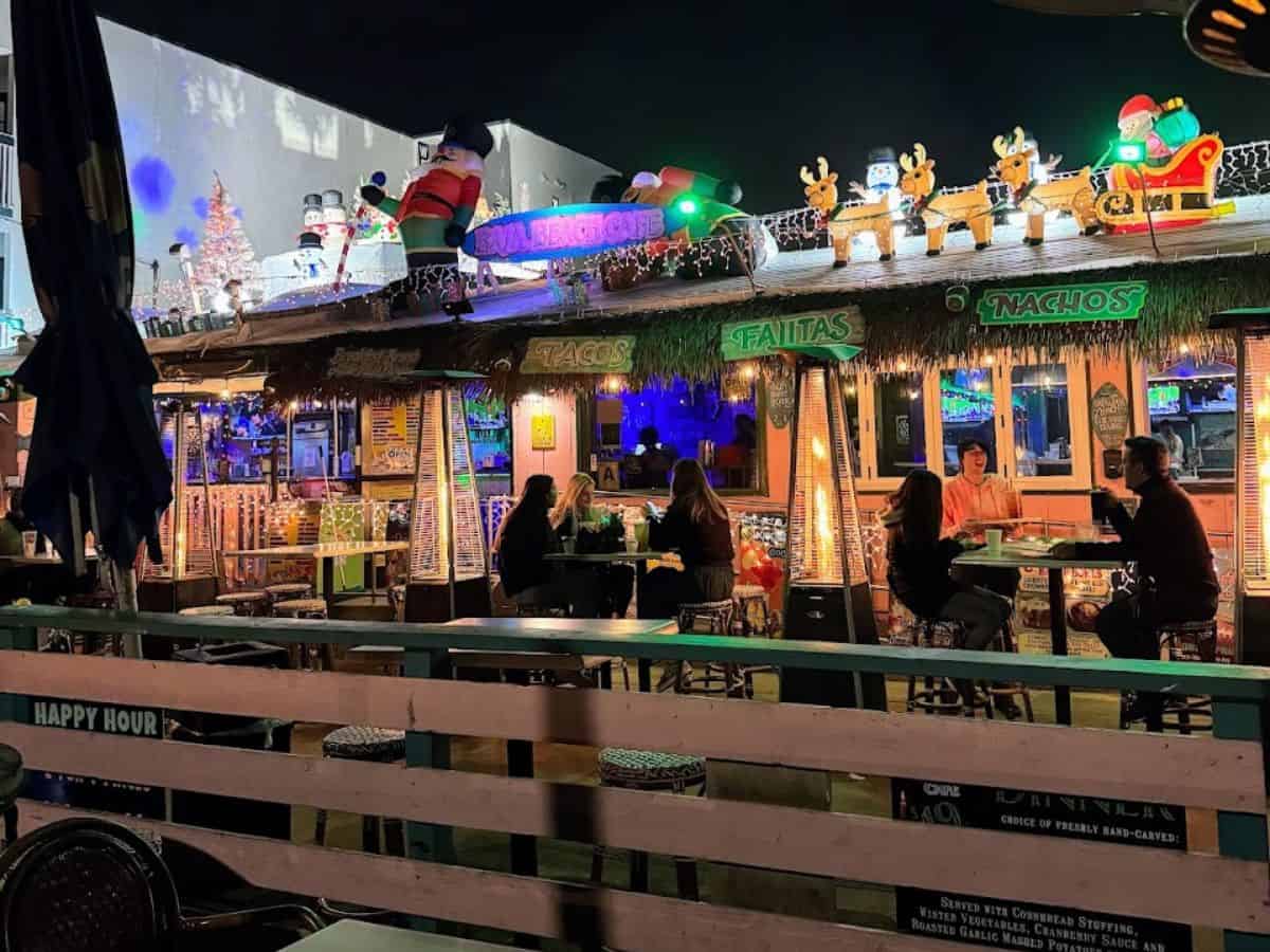 The vibrant nightlife of Pacific Beach San Diego is encapsulated in this photo, featuring an outdoor bar adorned with Christmas and cartoon decorations, twinkling lights, and a lively crowd gathered around tables, showcasing the festive spirit that makes it one of the best bars in the area