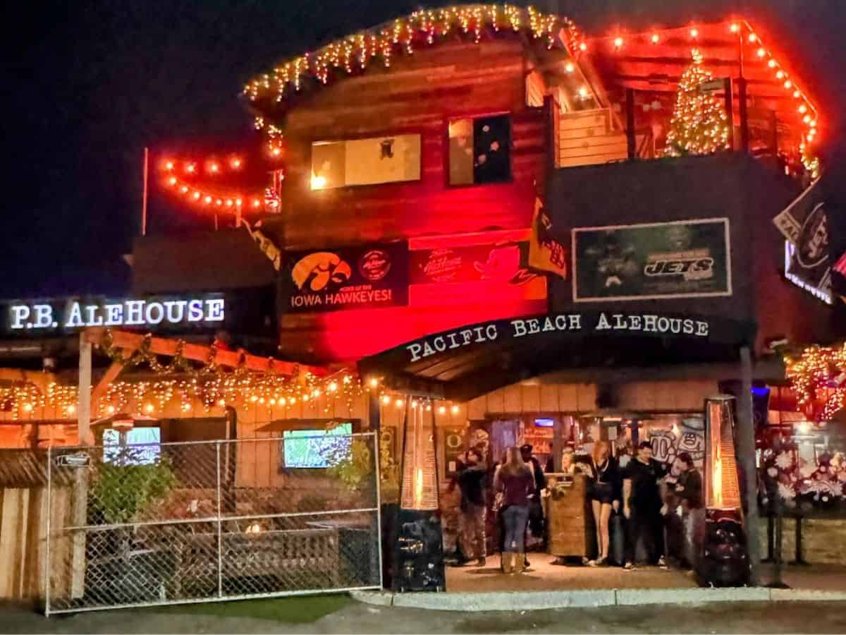 This wide shot of the 'Pacific Beach Alehouse' at night shows its distinctive architecture with strings of lights, Christmas trees, and festive decorations visible on its multi-tiered structure. It's a snapshot of the charm that places it on the list of the best bars in Pacific Beach San Diego